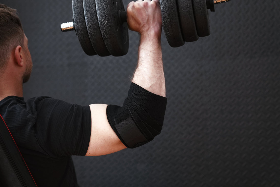Black 7mm elbow sleeves next to rolled elastic elbow wraps on a weight bench beside a loaded barbell
