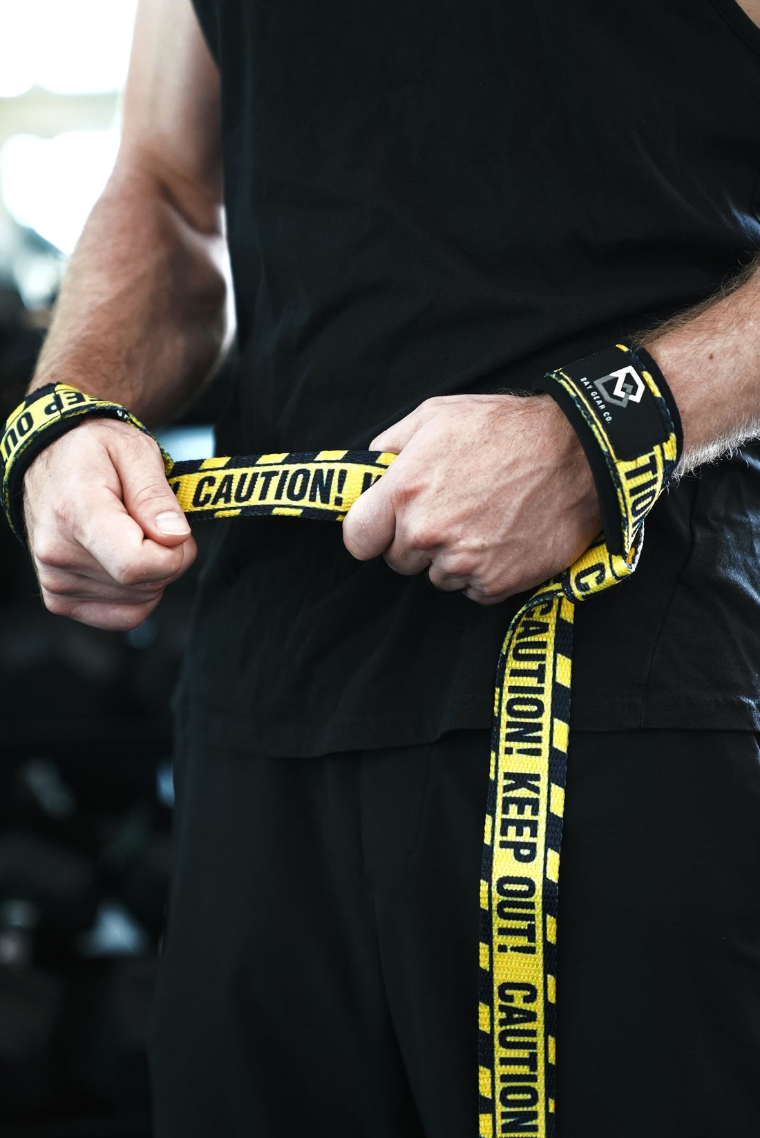 Lifter wearing Caution lifting straps on both wrists with the tails hanging